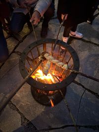 Menschen rösten Stockbrot über einem Feuerkorb draußen auf Steinboden