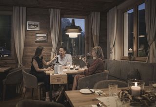 Drei Personen trinken Wein und unterhalten sich in einem gemütlichen Restaurant mit Holzdekor.