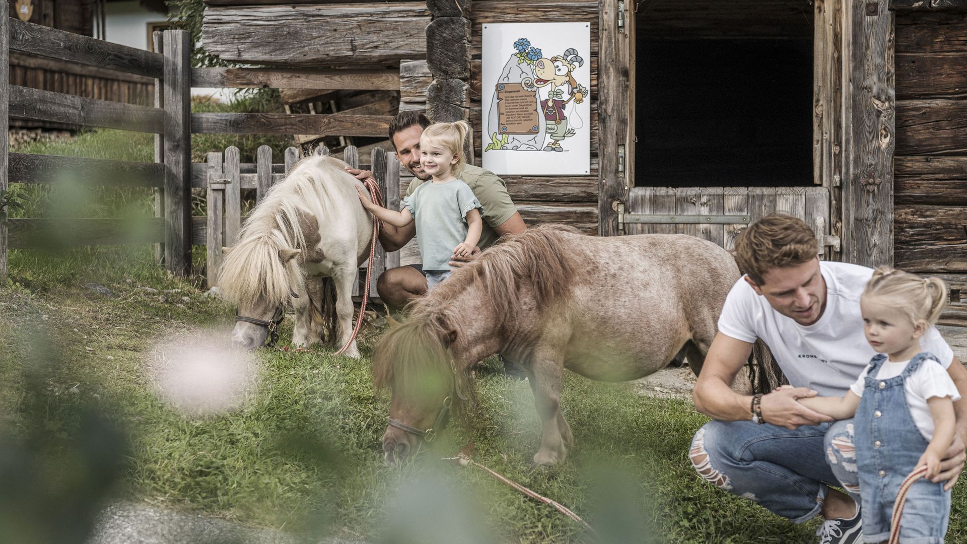 Farm Resort Geislerhof Zwei Väter mit kleinen Kindern und zwei Ponys neben einem Holzstall